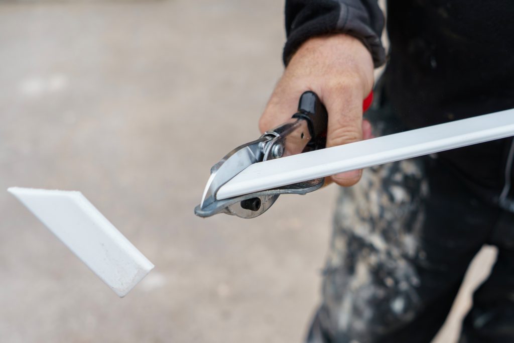 Close-up of a worker using Xpert Mitre Shears (or Gasket Shears) to cut a white UPVC trim piece.